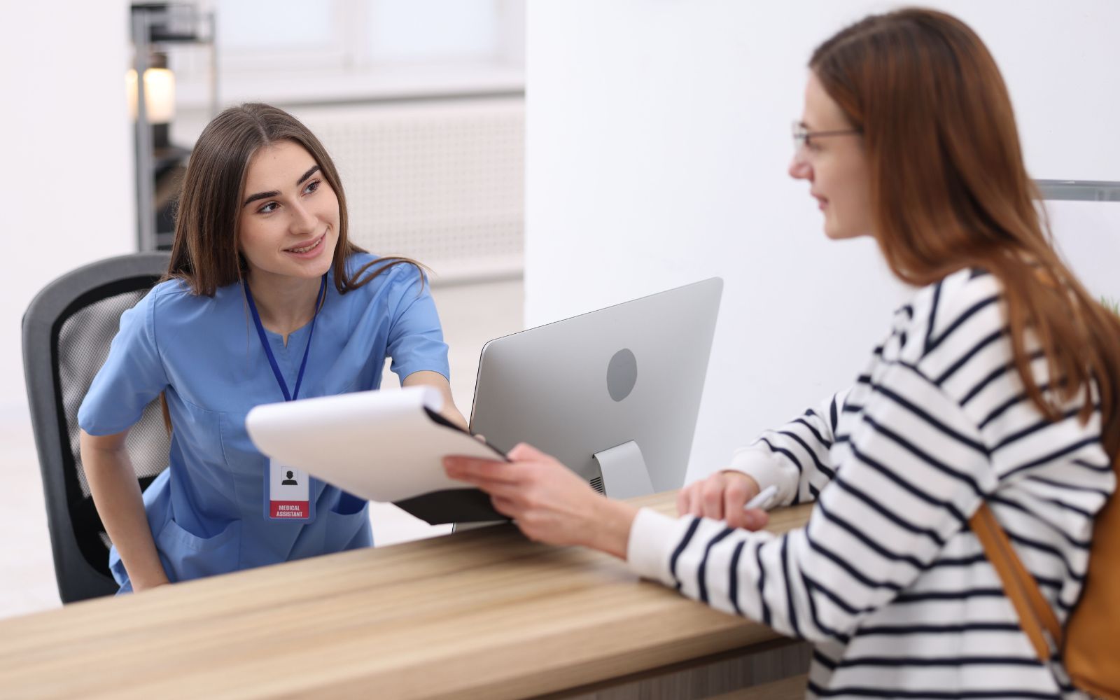 Clinic receptionist helping a patient at the front desk